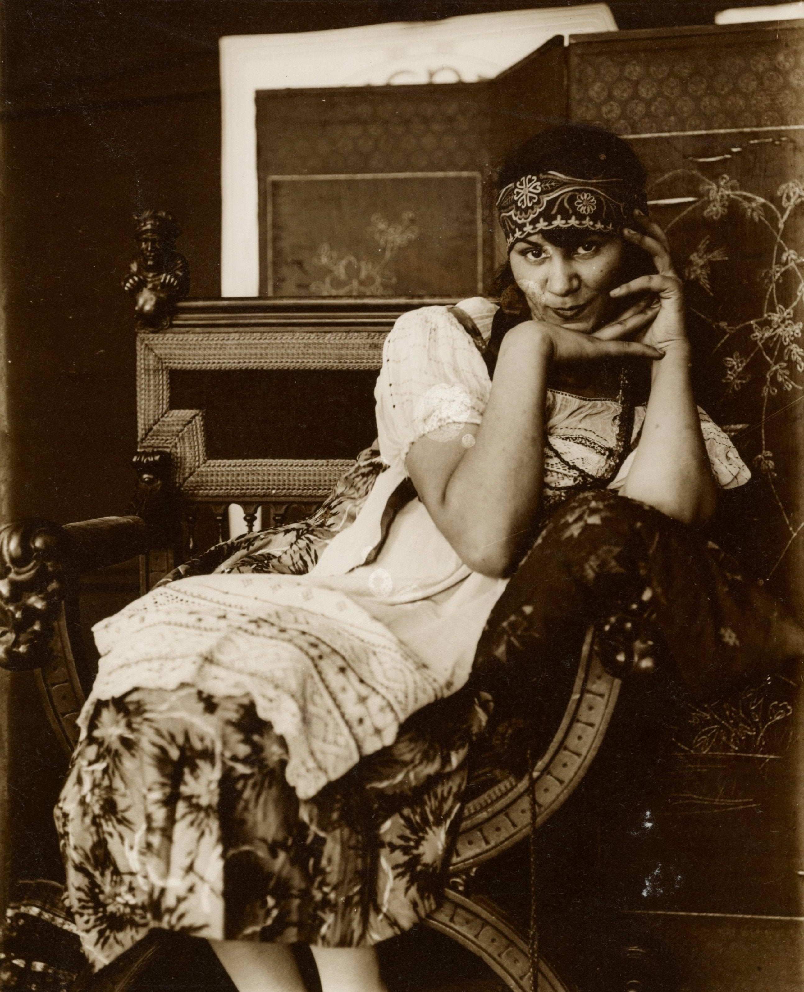 Black and white photograph of a female model sitting in a chair wearing a national costume with floral patterns.